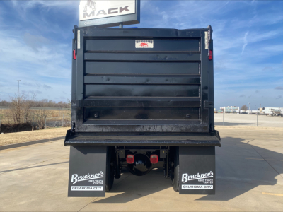 Back of a Volvo dump truck with a large black dump bed and red taillights; mud flaps show Buckner's Oklahoma City; clear blue sky.