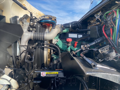 Engine bay of a Volvo VHD84F200 dump truck showing various hoses, a green fuel filter, red cap, black intake manifold, and warning sticker.