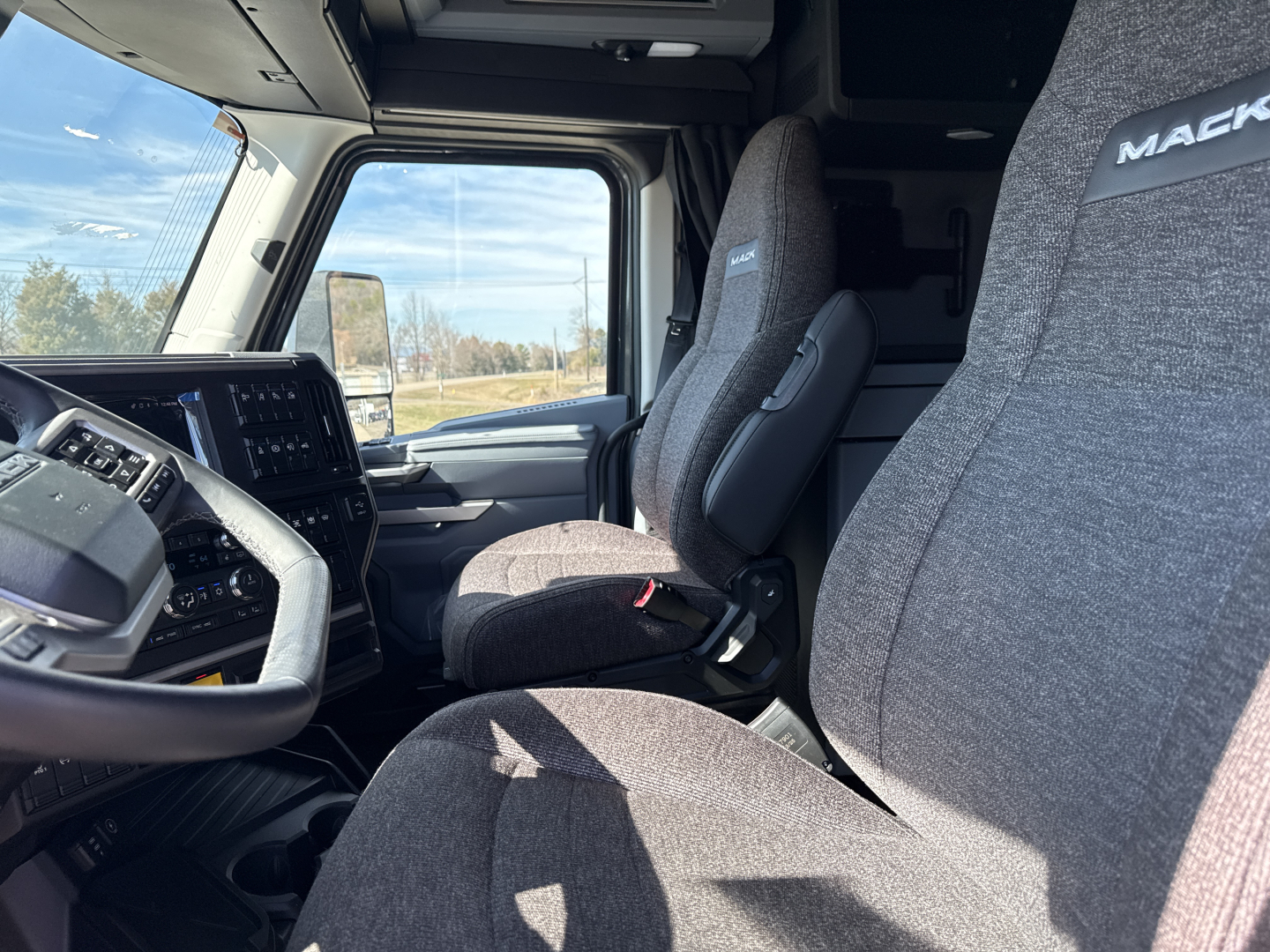 Cab interior of a 2026 Mack PR64T76H showing driver and passenger seats with Mack branding on headrests, steering wheel, and dashboard visible.