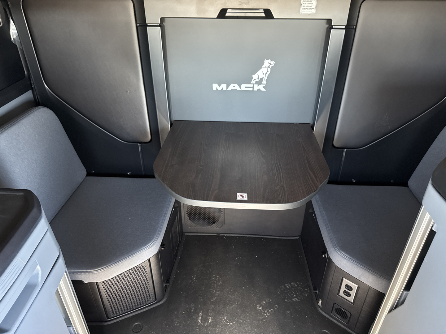 Mack PR64T76H truck cab interior with seating area and table showing Mack logo on back panel.