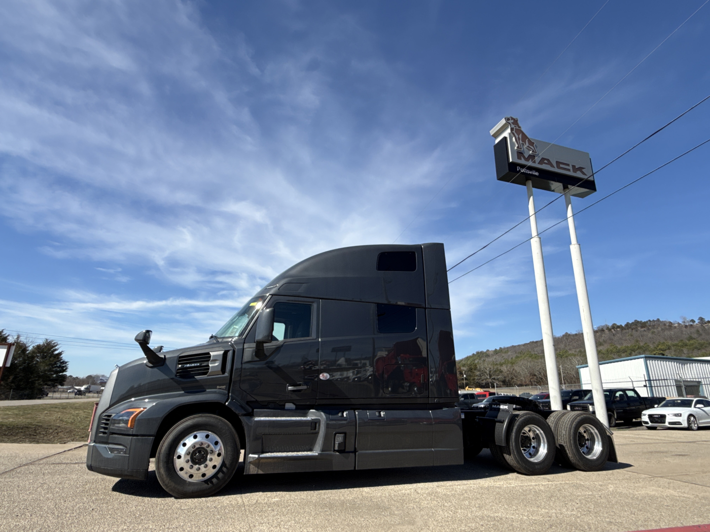 2026 Mack PR64T76H tractor in a parking lot showing a high-roof sleeper cab, black exterior, dual rear axles, and Mack dealership sign in background.