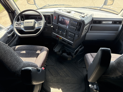 Inside view of a 2026 Mack PR64T76H cab showing steering wheel, dashboard with display screen, and driver and passenger seats.
