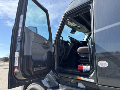 Mack PR64T76H truck cabin with door open showing interior and dashboard, exterior gray paint with certification sticker and engine start area.