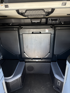 Cab interior of a new Mack PR64T76H showing a compact center console with storage, overhead dash area, and seating area around a metal access panel.