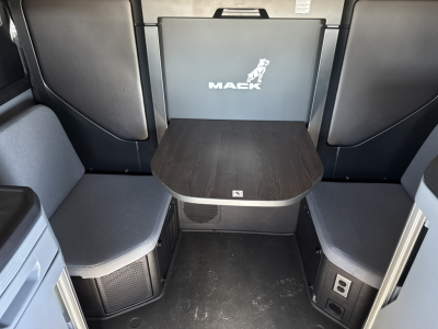 Mack PR64T76H truck cab interior with seating area and table showing Mack logo on back panel.