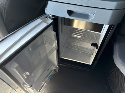 Mack PR64T76H truck interior showing open under-dash refrigerator/freezer unit with empty freezer compartment and door shelves.