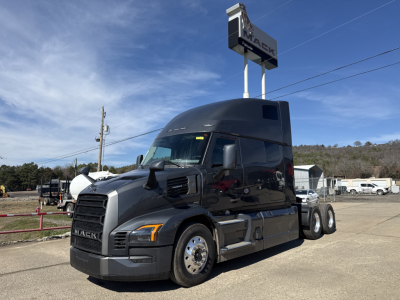 Mack PR64T76H conventional sleeper truck in a dealership lot, dark gray exterior, cab front grille, side view with sleeper cab and dual rear axles.