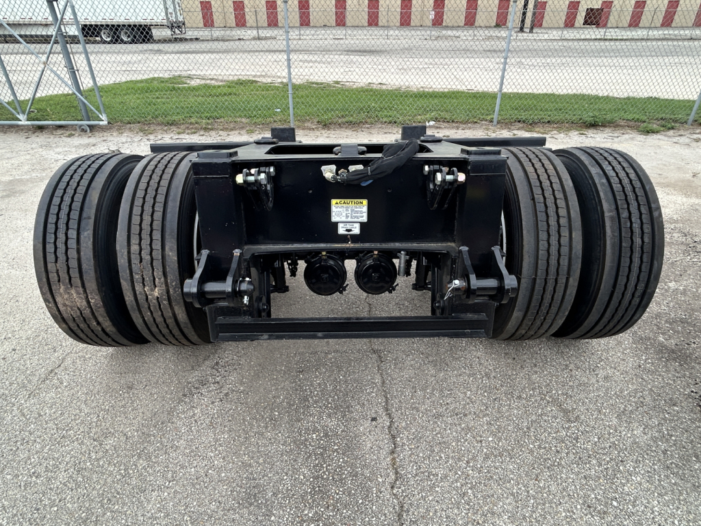 Trailer flip-axle assembly showing dual tires, black metal frame, and hitch area with label visible.