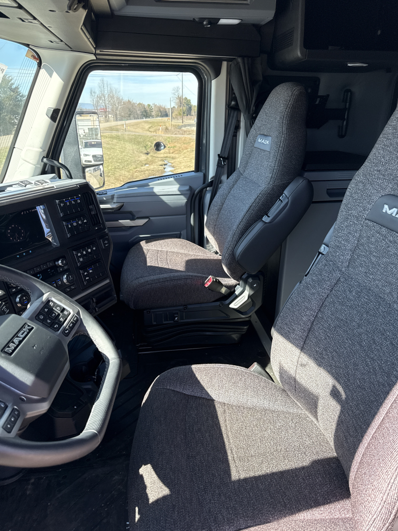 Cab interior of a 2026 Mack PR64T76H showing driver and passenger seats, dashboard, steering wheel, and large windshield.
