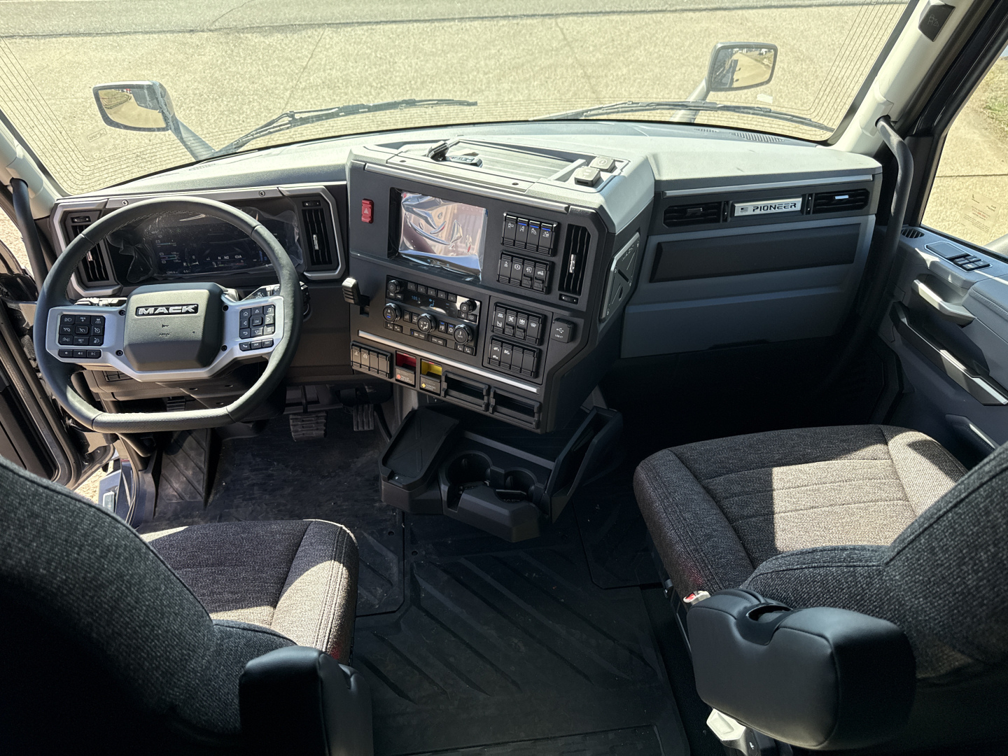 Mack PR64T76H truck cab interior showing steering wheel and digital dashboard with multiple controls and center console.