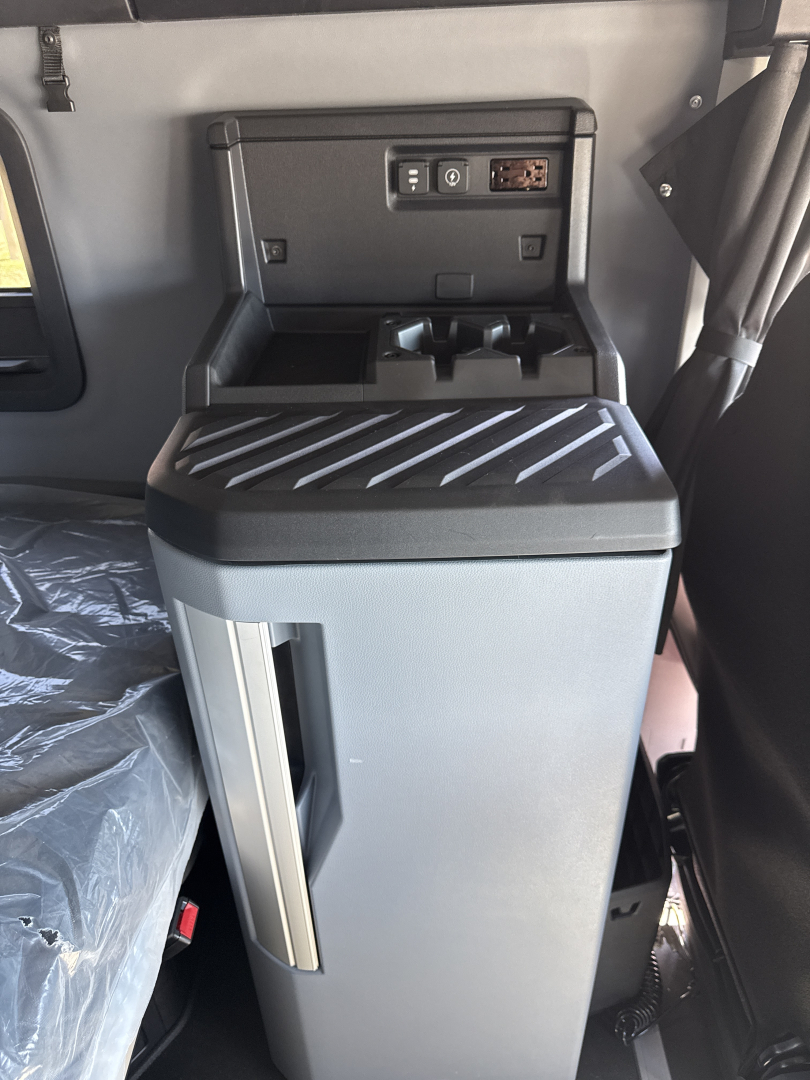 Cab interior of a 2026 Mack PR64T76H showing center console with cup holders and control panel; vertical storage pocket on door and ribbed surface on top.