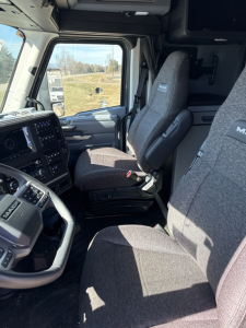 Cab interior of a 2026 Mack PR64T76H showing driver and passenger seats, dashboard, steering wheel, and large windshield.