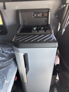 Cab interior of a 2026 Mack PR64T76H showing center console with cup holders and control panel; vertical storage pocket on door and ribbed surface on top.