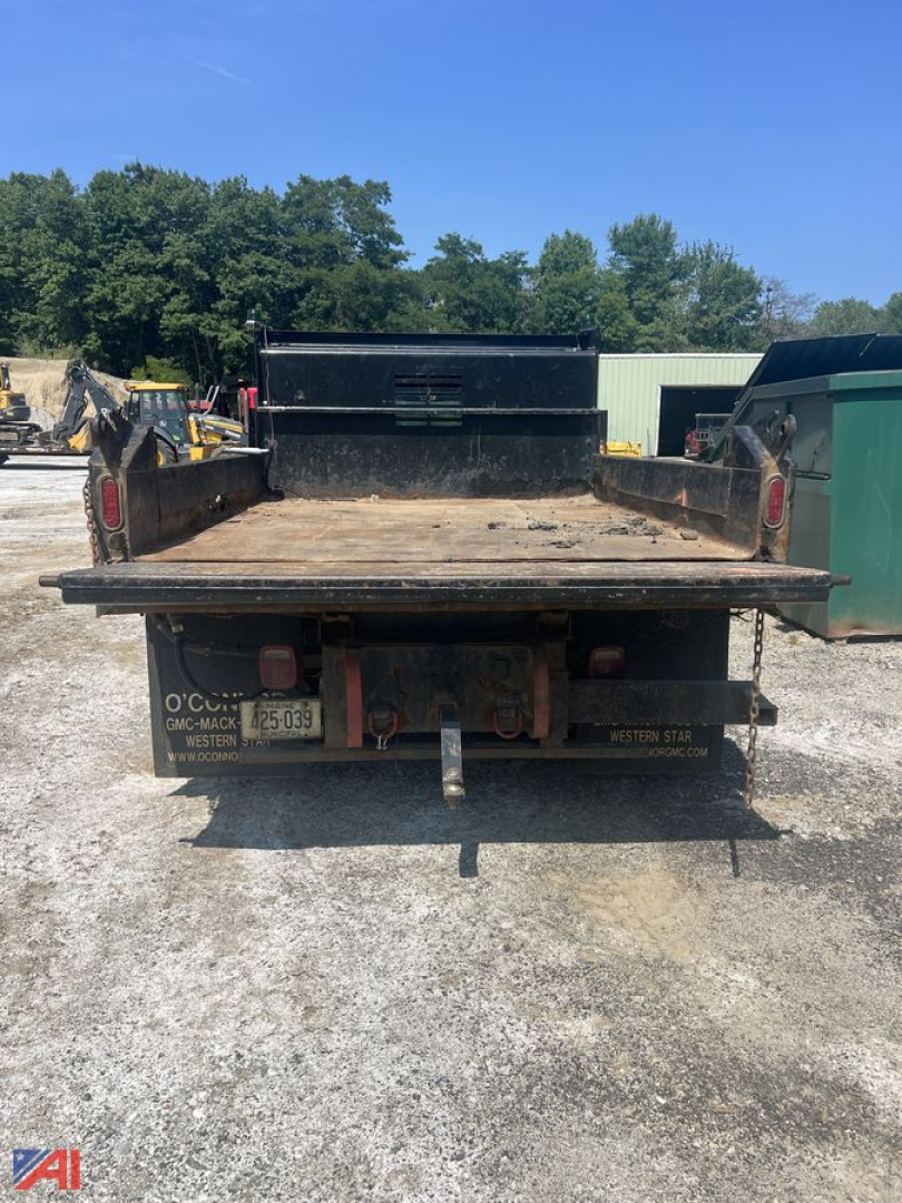 Dump truck bed view showing flatbed with tailgate and hitch, rear lights, and license plate area.