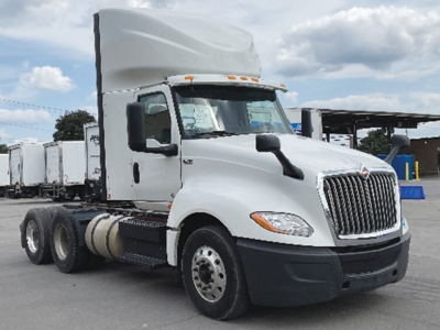 Truck cab showing International LT625 with sleeper, front grille, dual rear axles, and fuel tanks; windshield tag visible.
