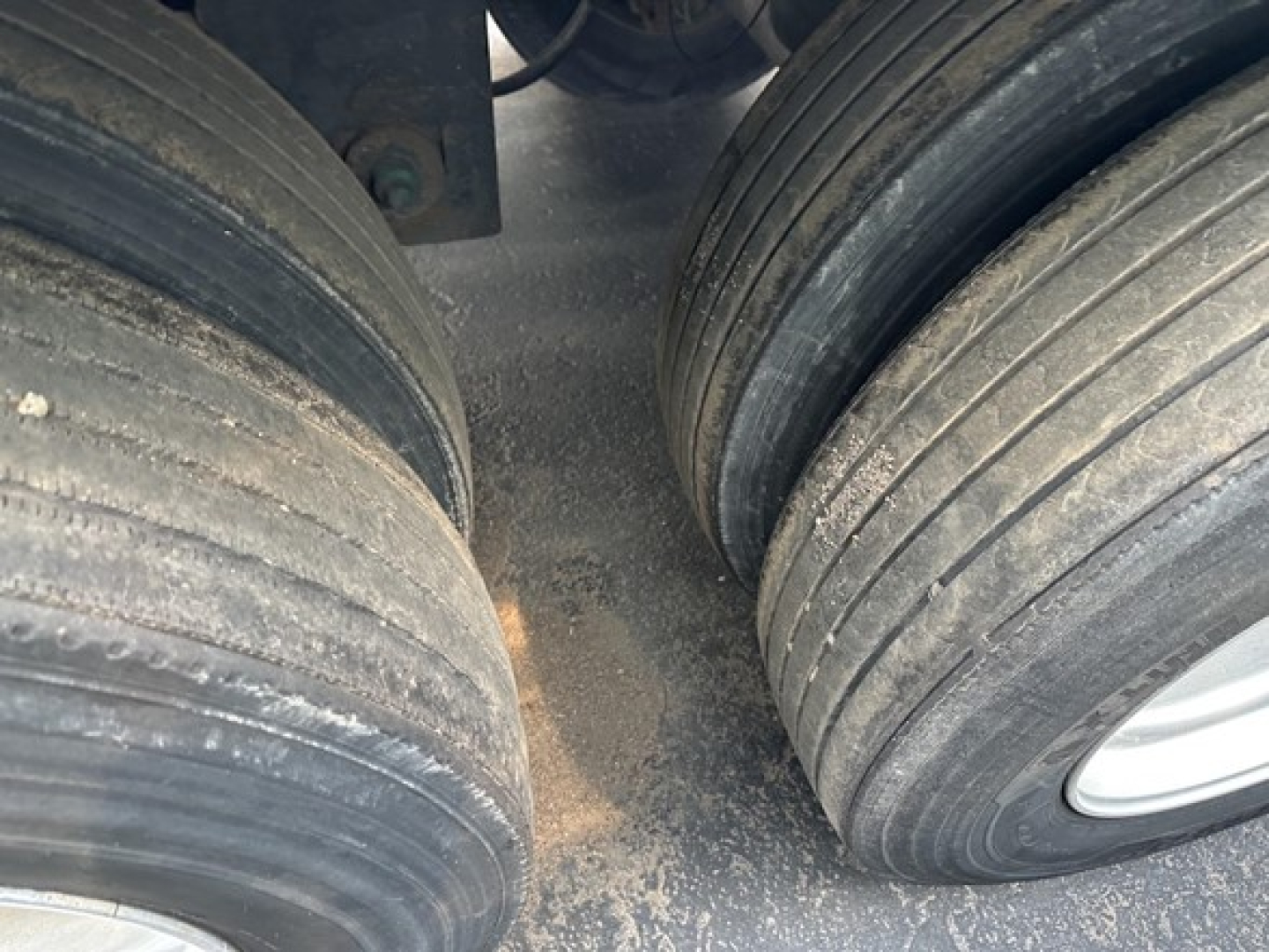 Trailer dual rear wheels with heavy wear on rubber tires and dirt on the ground beneath.