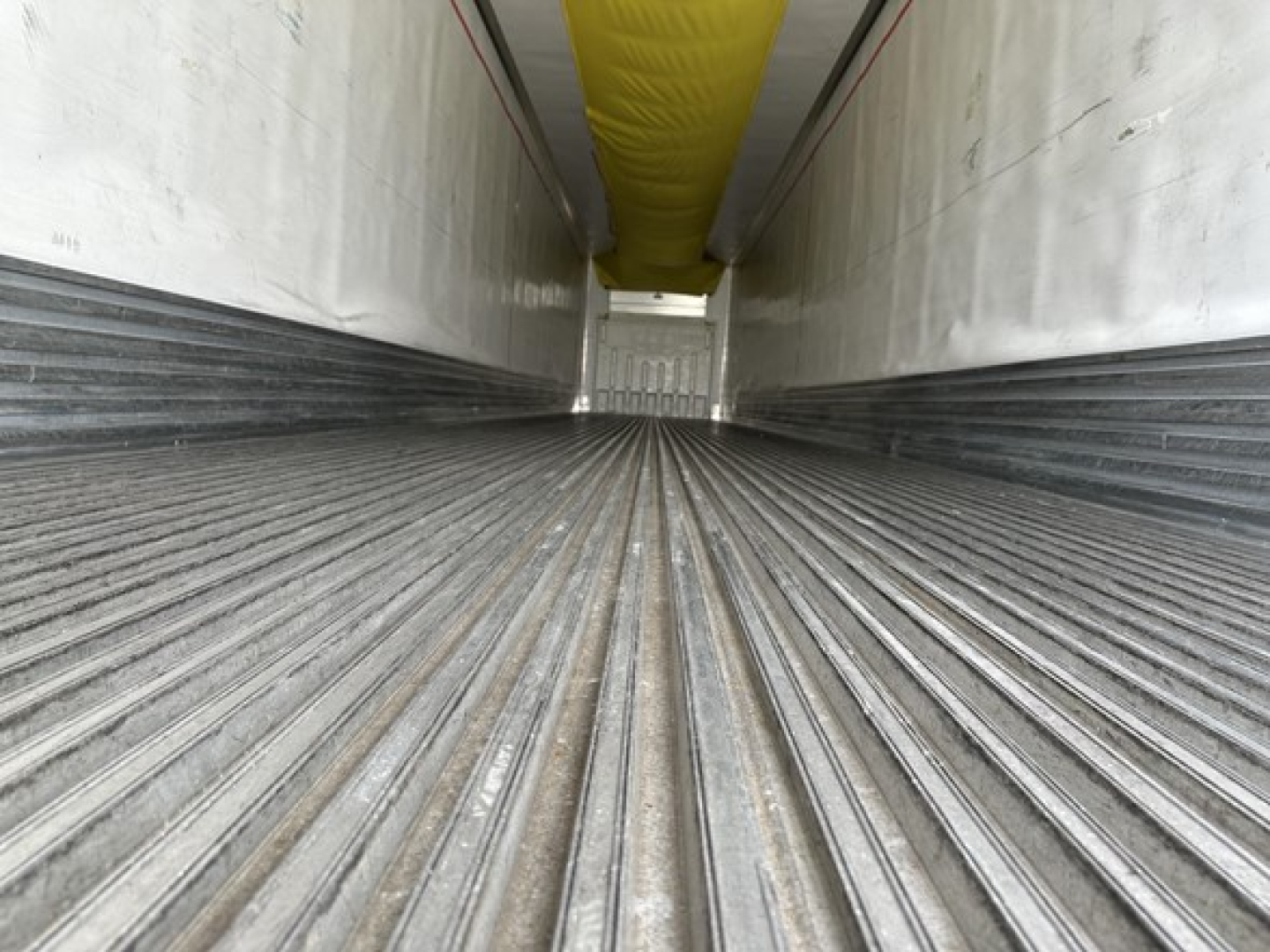Trailer interior showing ribbed metal floor and white sidewalls with a yellow ceiling duct, long aisle view