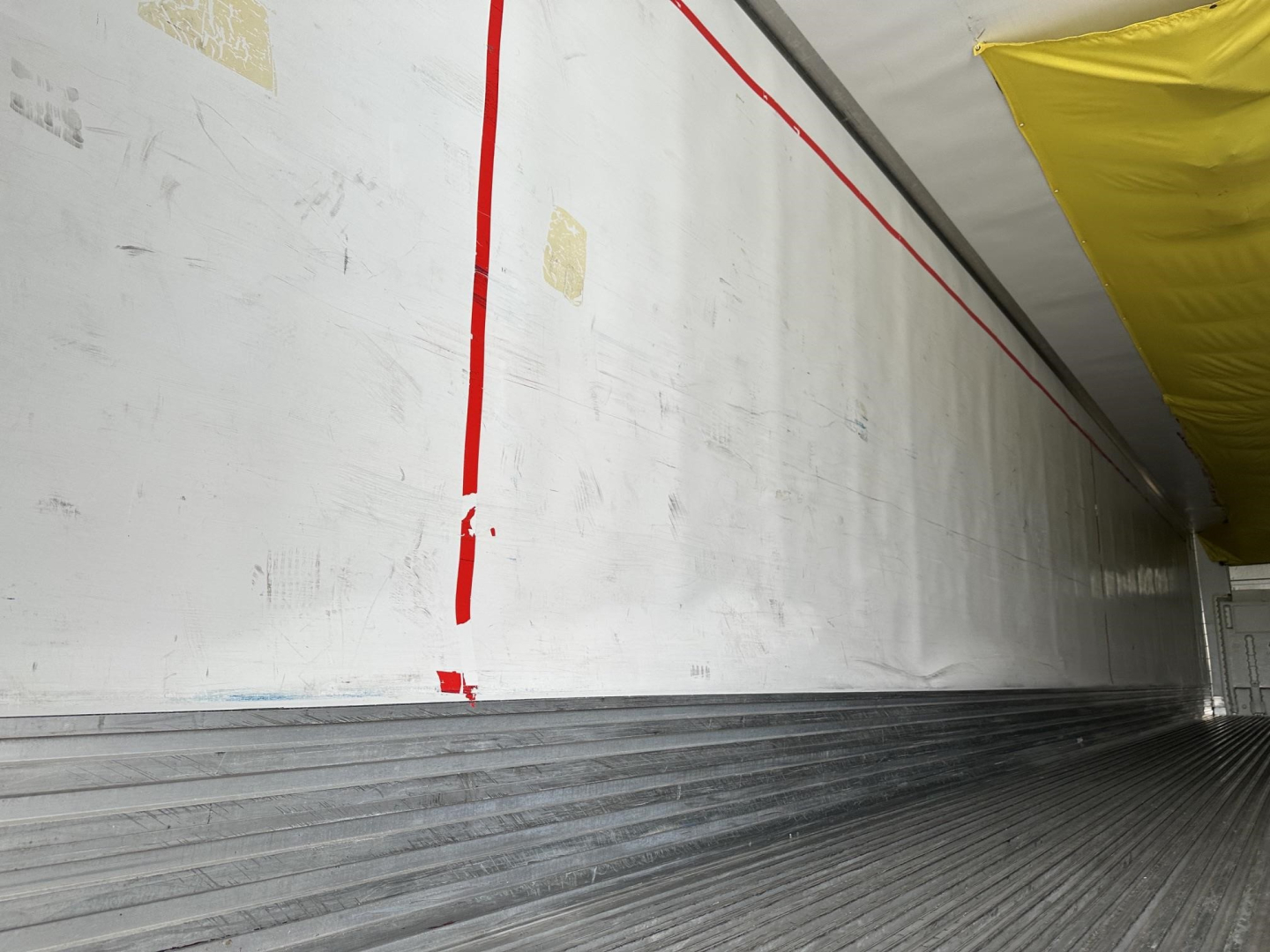 Trailer interior sidewall and floor showing aluminum wall with red vertical stripe and ribbed metal floor panels.