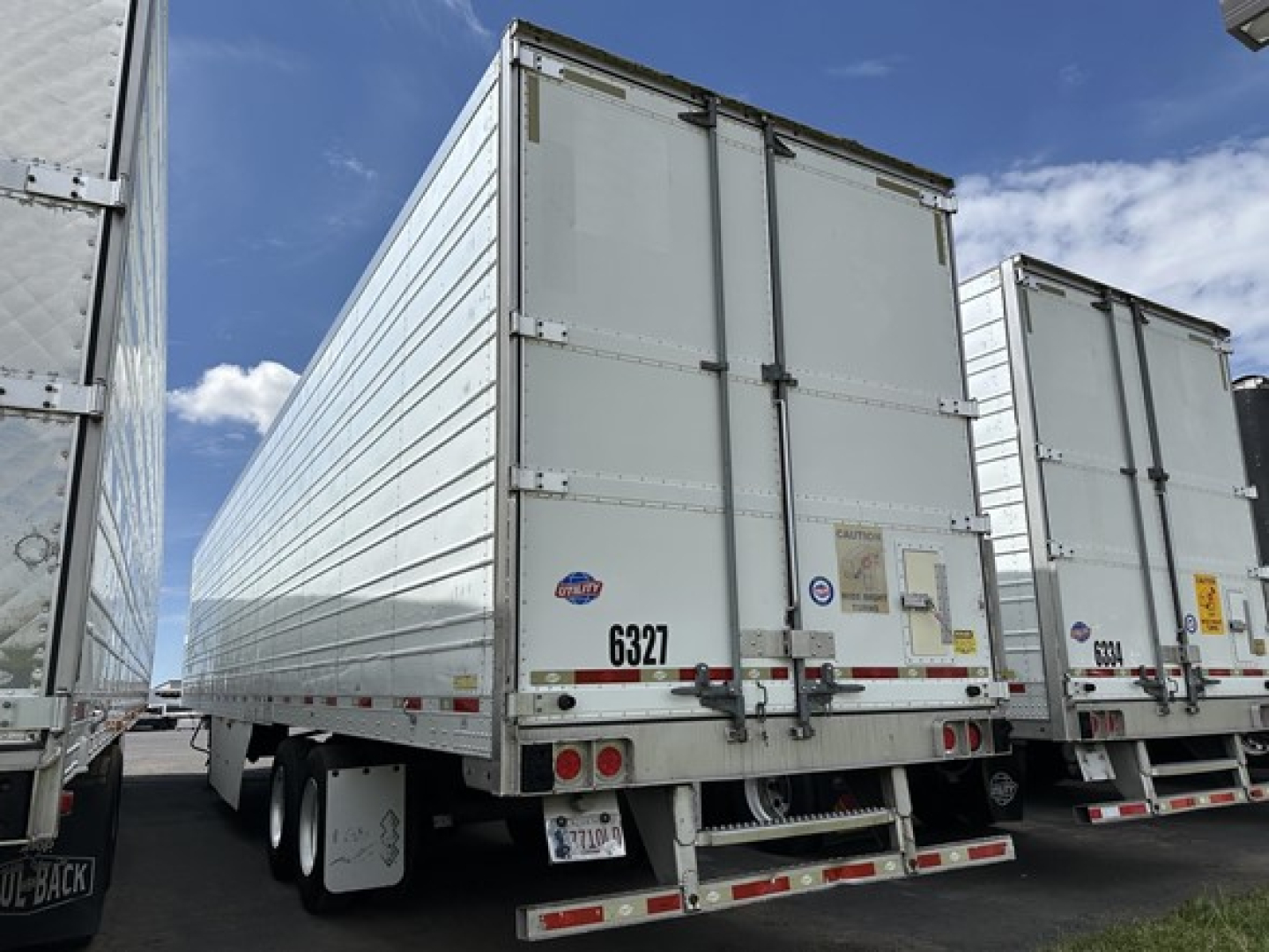 Trailer rear view showing large white refrigerated box with double doors and multiple halogen tail lights, tandem axle trailer undercarriage visible.