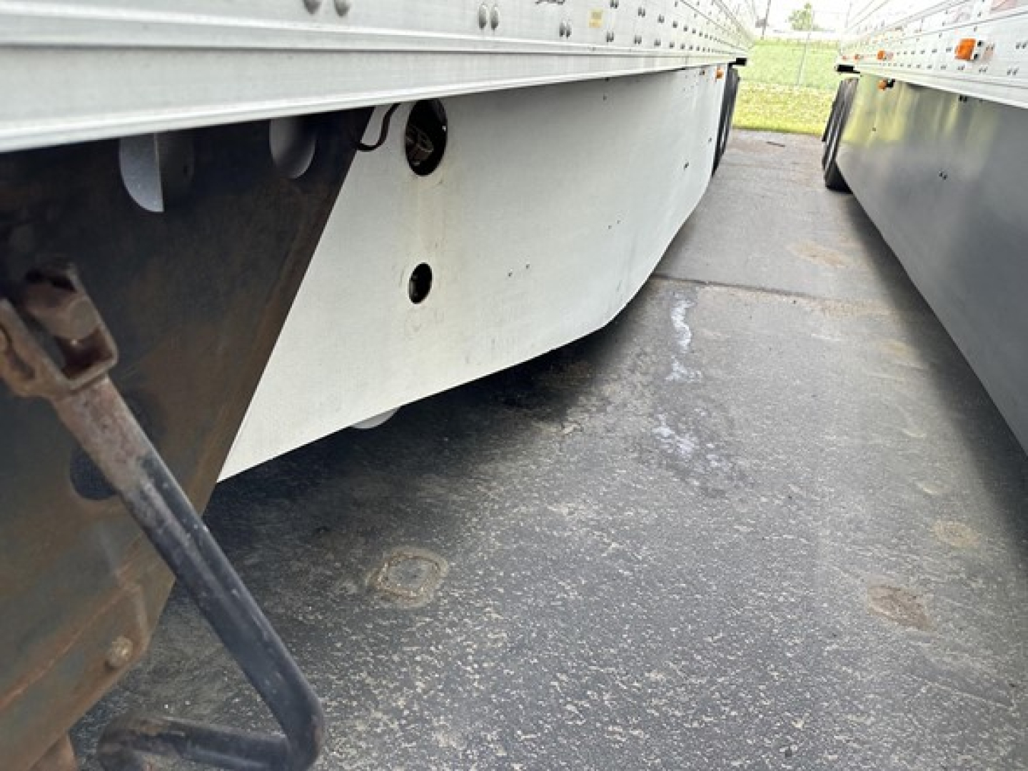 Trailer undersideView shows a silver box with round hole and support bracing. Close-up of lower sidewall showing metal framework and dirt path.
