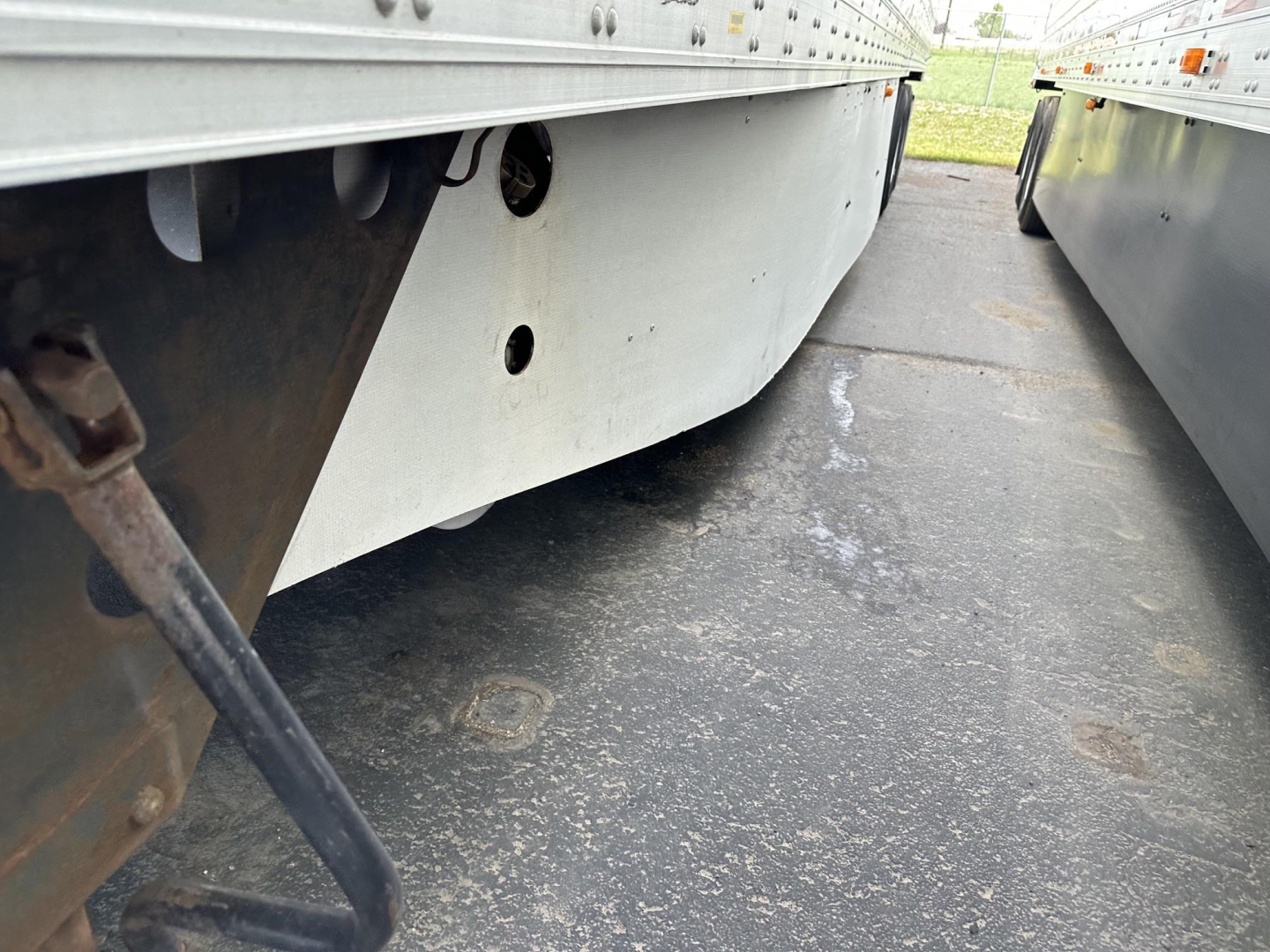 Trailer undercarriage showing side skirt and support braces of a 2015 Utility 3000R reefer trailer, with concrete ground and adjacent trailer.