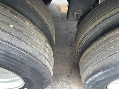 Trailer axles showing dual city tires in contact with the road surface, visible tread wear, and dirty frame area between wheels.