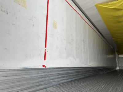 Trailer interior side wall with ribbed cargo floor showing white paneling and yellow corner tarp; no legible branding or numbers readable.