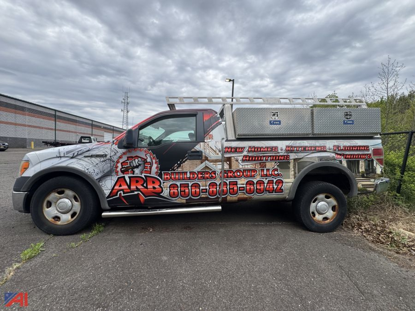 Ford F-150 pickup truck in-service side view with service utility box and ladder rack, logo graphics on door, text on vehicle reading ARB Builders Group and contact number.