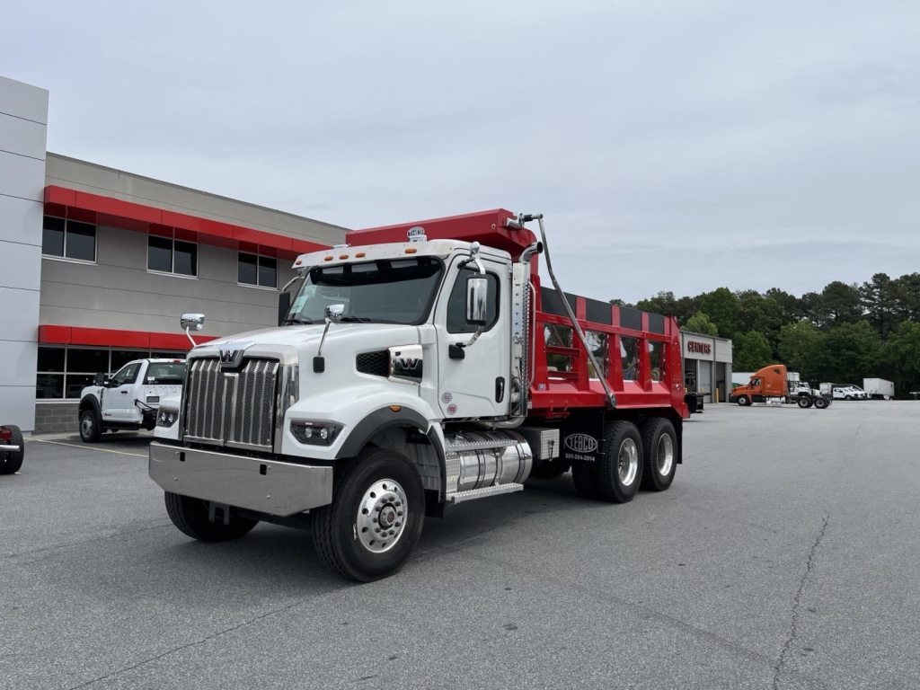 Western Star 47X dump truck in white cab and red dump bed, front three-quarter view, dealership lot in background.