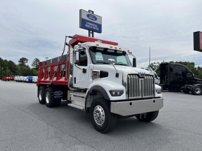 Western Star 47X dump truck in front of dealership lot, white cab with chrome grille, red dump body, dual rear axles, Ford dealership sign in background.