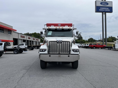 Front view of a 2027 Western Star 47X dump truck with large chrome grille, headlights, and orange light bar on cab, dealership lot in background.