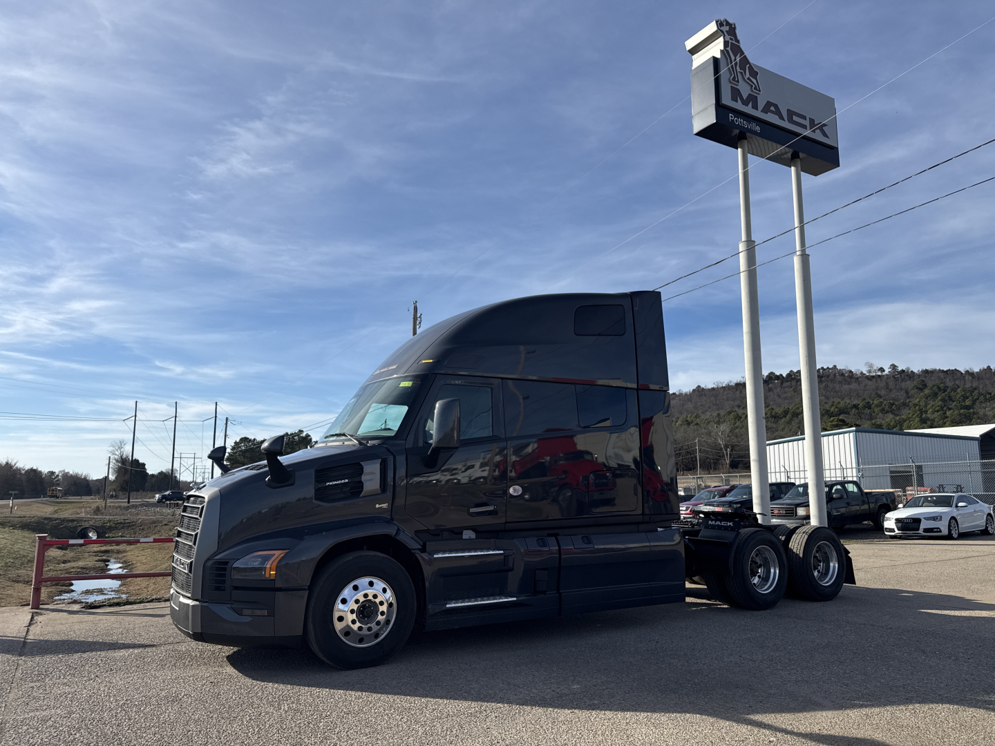 Truck side view showing a black 2026 Mack PR64T76H conventional sleeper tractor with dual rear axles and chrome wheel covers.