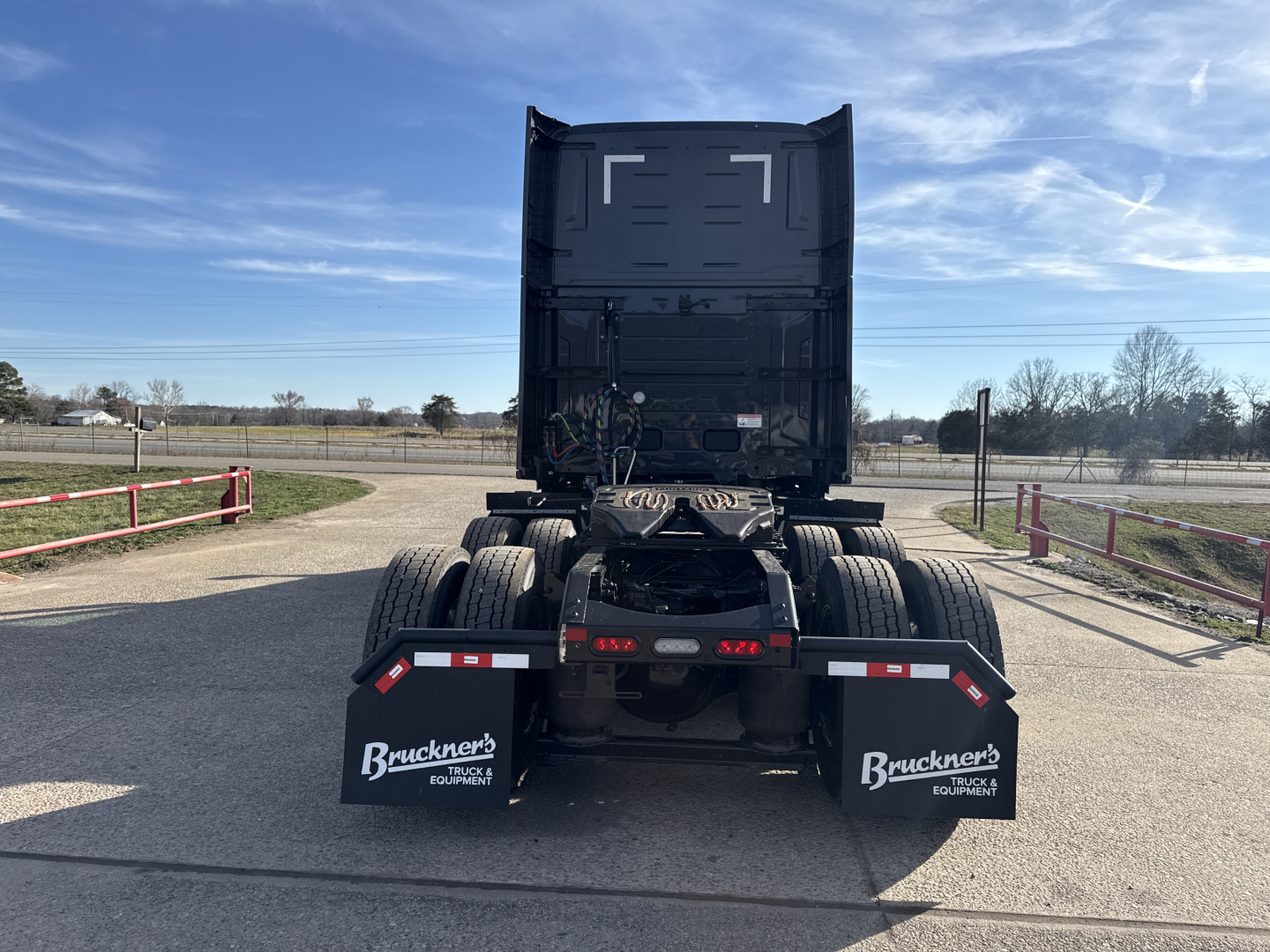 Truck rear view showing fifth wheel, dual rear axles, and mud flaps with Buckner's Equipment logos under a raised sleeper cab on a dealership lot.
