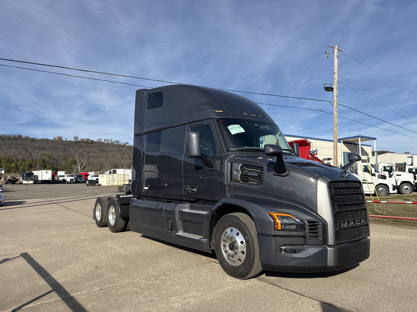 Truck cab overview showing a dark gray Mack PR64T76H sleeper tractor with a high-roof bunk and 6x4 drivetrain, front-right view, badge details not legible.
