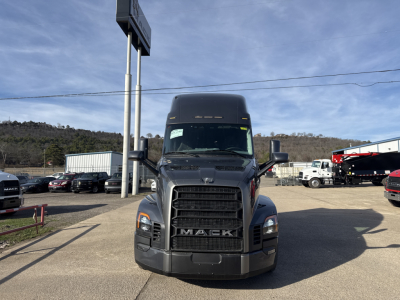 Front view of a Mack PR64T76H truck in a dealership lot. Prominent black grille with 'MACK' letters, large bumper, and tall sleeper cab. Windshield with wipers, side mirrors, and surrounding dealership vehicles.