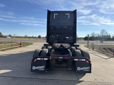 Truck rear view showing fifth wheel, dual rear axles, and mud flaps with Buckner's Equipment logos under a raised sleeper cab on a dealership lot.