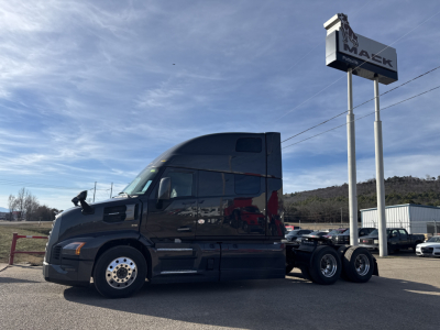 Truck side view of a new 2026 Mack PR64T76H conventional sleeper tractor with a dark exterior, showcased at a dealership lot.