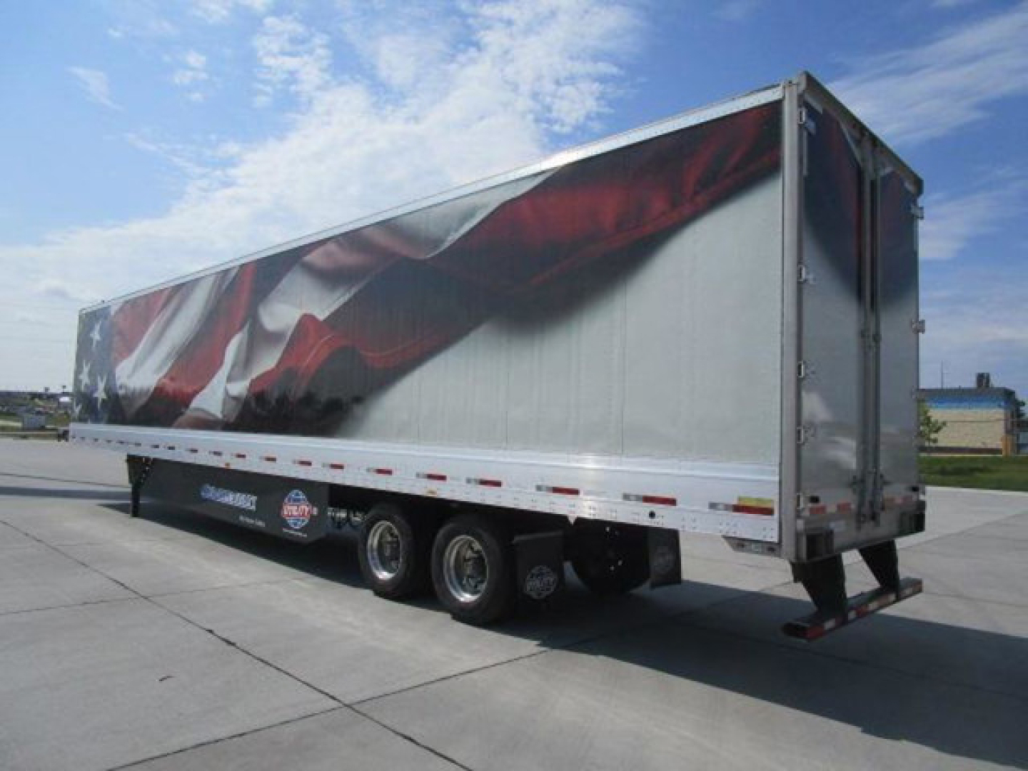 Trailer side view showing a utility van trailer with patriotic graphic on the curtain and dual rear axles.