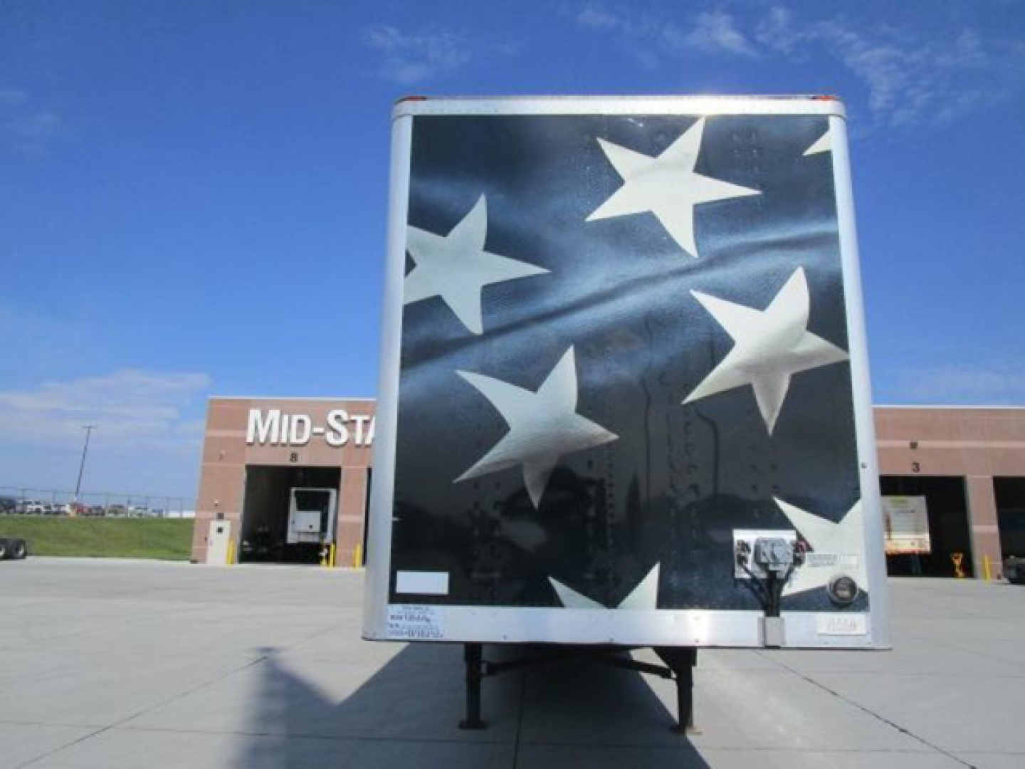 Trailer back showing a black surface with white stars, rear door latch, and trailer support legs under the bumper.