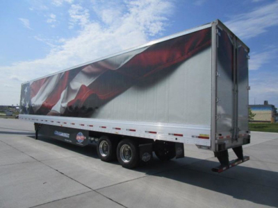 Trailer side view showing a utility van trailer with patriotic graphic on the curtain and dual rear axles.