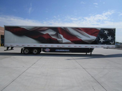 Trailer with American flag graphic on side showing logo and text; side of trailer with dual rear axles and support legs; graphic spans length