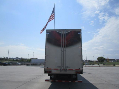 Truck trailer rear view showing vertical double doors, chain bars, and taillights in a parking lot with an American flag overhead.