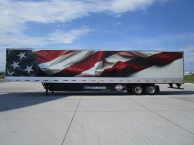 Trailer side view with a large American flag graphic, dual rear wheels, and streamlined trailer body.