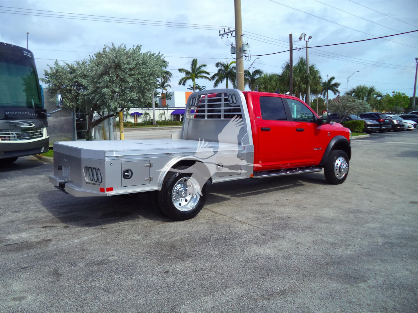 2024 Ram 5500 SLT flatbed truck side view showing red cab and aluminum flatbed with storage boxes