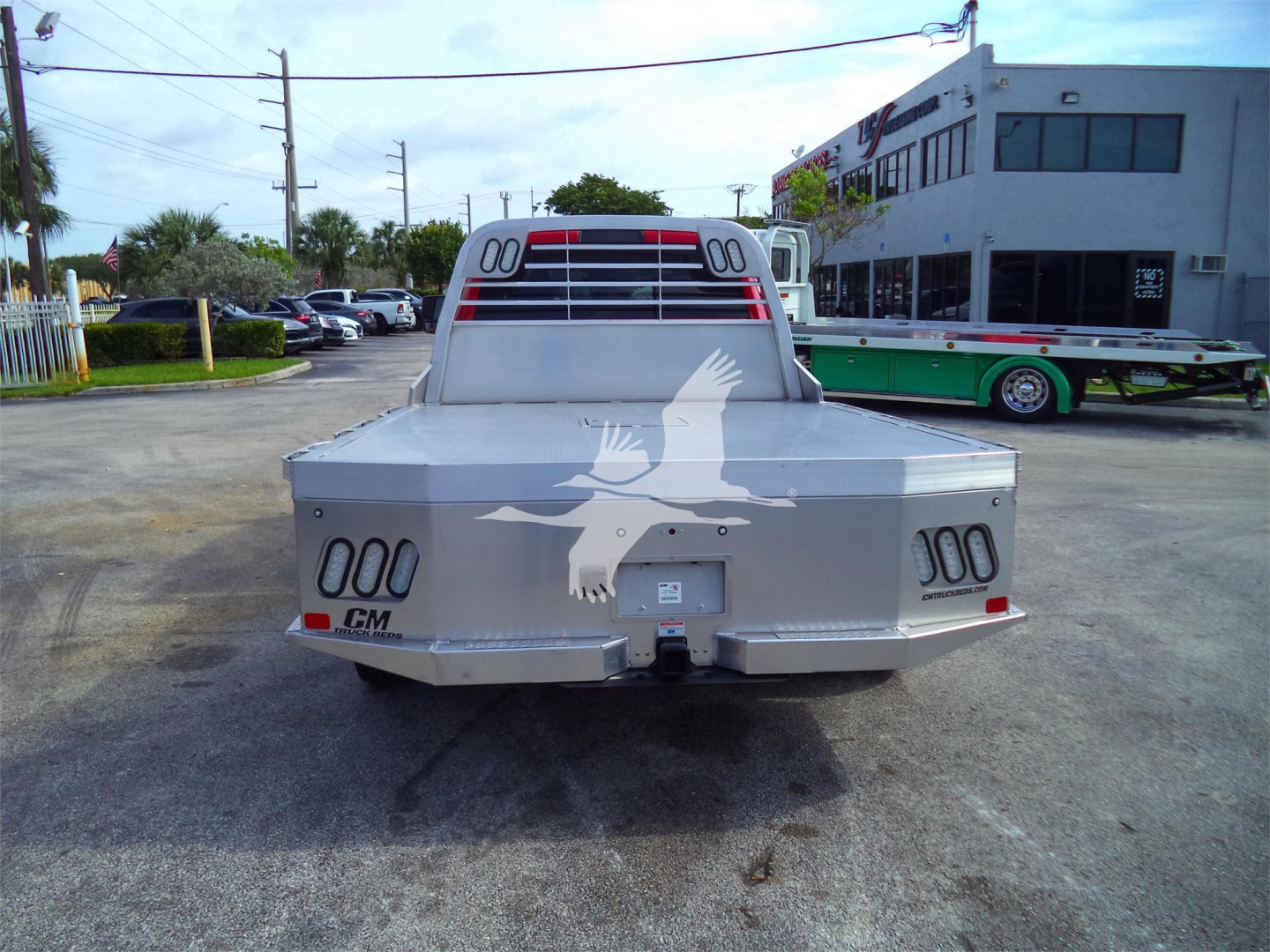 Rear view of a 2024 Ram 5500 SLT flatbed truck in a dealership lot showing taillights, bumper, and flatbed with a graphic eagle logo on the tailgate.