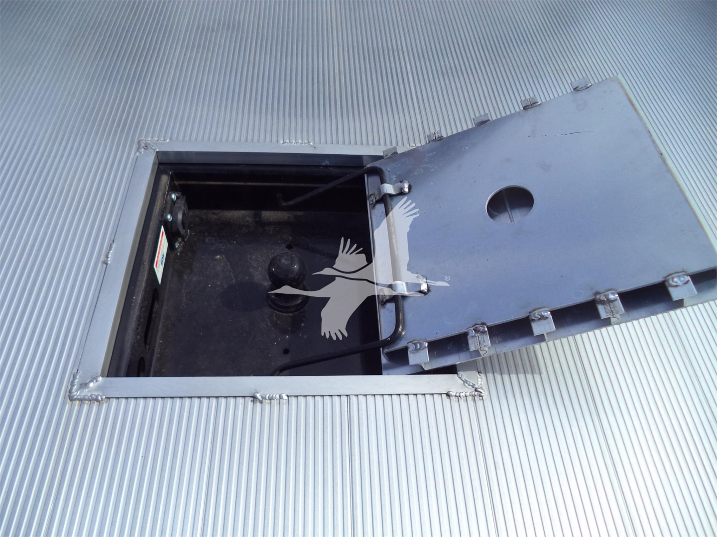 Ram 5500 truck bed hatch opening showing interior access with latch; metal ribbed surface surrounding and hinged lid raised.