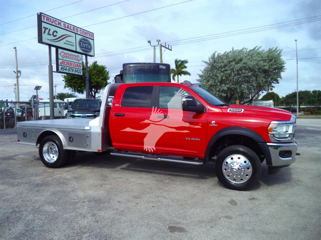 Red Ram 5500 SLT pickup with flatbed and chrome wheels, dealership lot in background with TLC sign. Vehicle shows RAM badge and service graphics on door and bed.