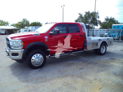 Ram 5500 flatbed truck in red with white wings graphic on door, chrome front, long dual rear wheels, aluminum flatbed with toolbox; no visible liquid labels.