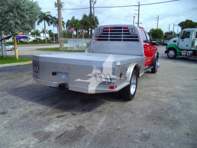 Ram 5500 flatbed truck rear view with aluminum flatbed and black rear lights, light-colored cab in background, dealership lot setting.
