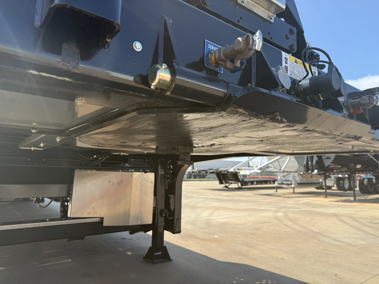 Trailer underside view showing coupling hitch, landing legs, and frame with safety decals on a Landoll 455B-53 traveling axle trailer.